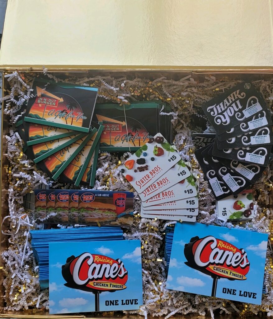Gift cards to In-n-out, Starbucks, State Bros., Jersey Mikes, and Raising Cane's are neatly arranged on  crinkle filler paper in opened box.